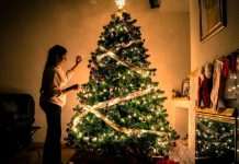 child standing in front of Christmas tree with string lights