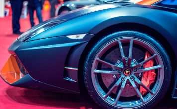Detailed view of a luxury sports car wheel on a red carpet at an auto show. Automechanika